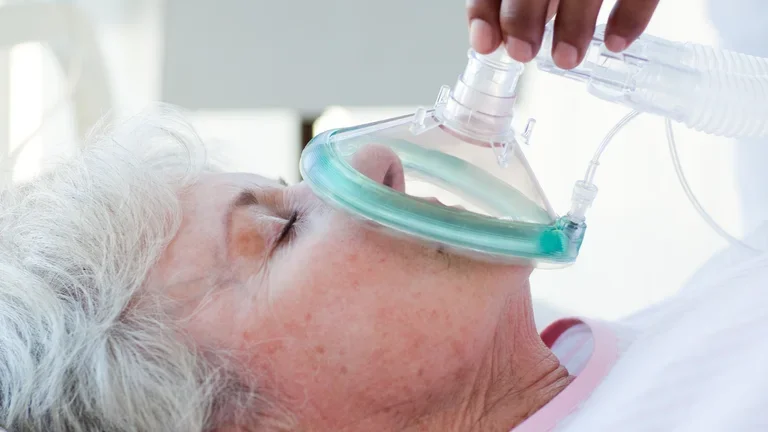 Frau die mit einer Maske beatmet wird und auf einem Bett liegt