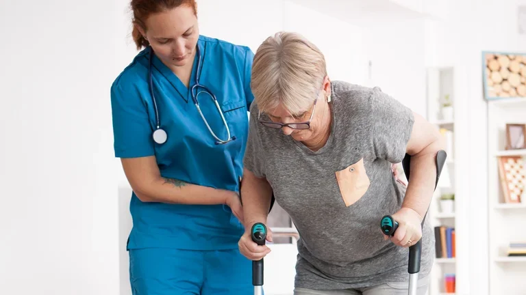 Pflegerin hilft einer Seniorin auf Krücken beim Gehen