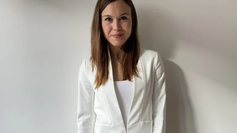 Eine Frau steht neben einem Stuhl auf dem ein Laptop und ein Notizbuch liegen