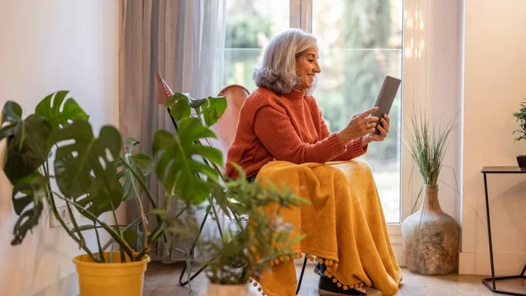 Ältere Frau sitzt auf einem Stuhl und liest einen Artikel