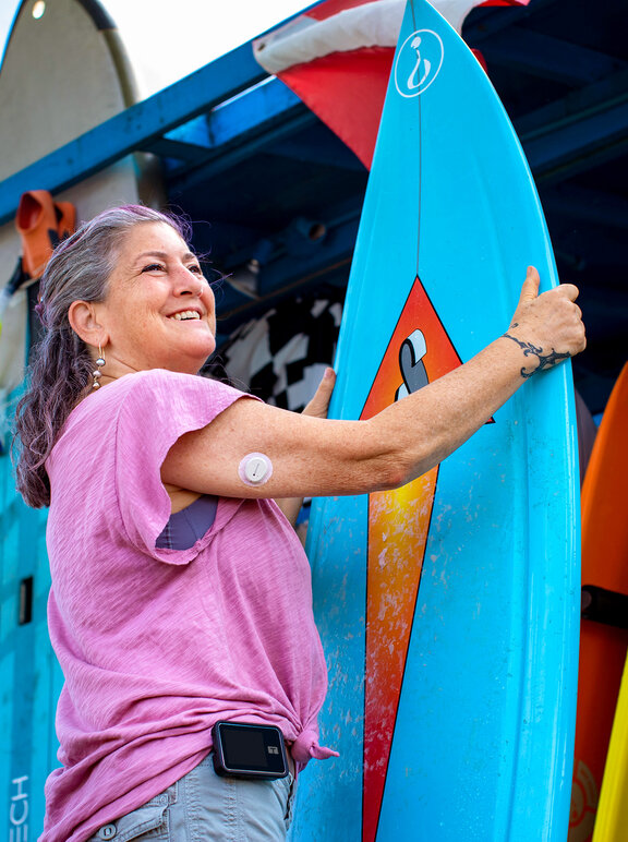 Diabetes Patientin mit Surfbrett am Strand