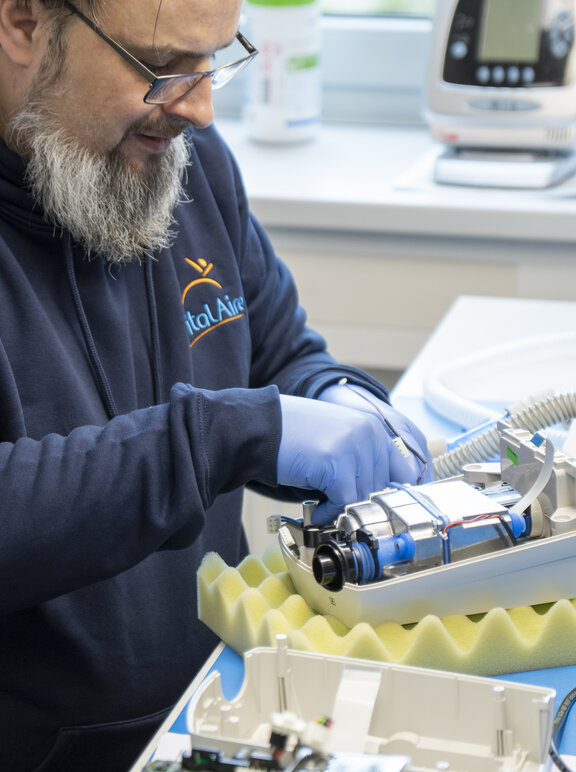 Mitarbeiter sitzt an einem Tisch und repariert ein technisches Gerät