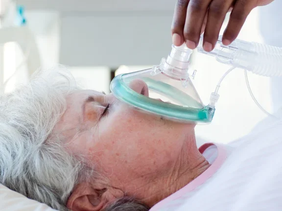 Frau die mit einer Maske beatmet wird und auf einem Bett liegt