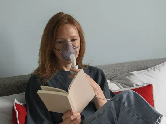 Eine Frau mit Sauerstofftherapie-Maske liest ein Buch