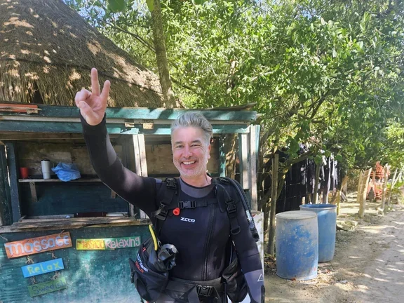 Maik steht in Taucherausrüstung vor der Kamera und hält zwei Finger hoch
