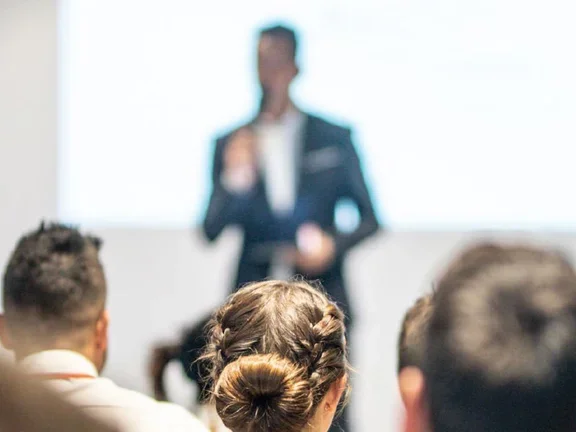 Eine vortragende Person steht vor sitzendem Publikum