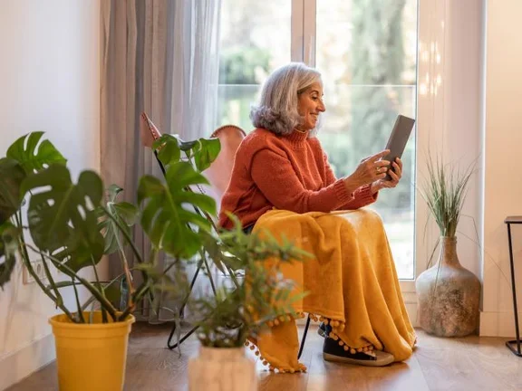 Ältere Frau sitzt auf einem Stuhl und liest einen Artikel