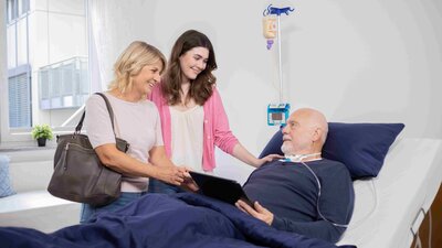 Zwei Frauen stehen am Bett eines Patienten in einer Intensivpflege-WG