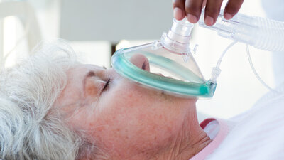 Frau die mit einer Maske beatmet wird und auf einem Bett liegt