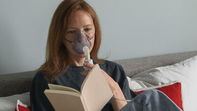 Eine Frau mit Sauerstofftherapie-Maske liest ein Buch