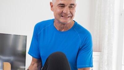 Ein Mann der am Bett eines Patienten steht und therapeutische Übungen durchführt