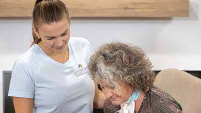 Eine Pflegerin steht neben einer Frau mit Rollator 