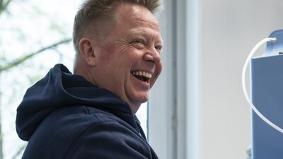 Ein Mann sitzt an einer Werkbank und lächelt