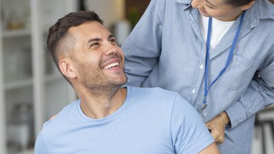 Eine Pflegerin schiebt einen Mann im Rollstuhl zuhause