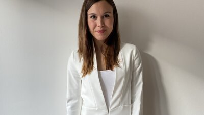 Eine Frau steht neben einem Stuhl auf dem ein Laptop und ein Notizbuch liegen