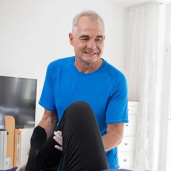 Ein Mann der am Bett eines Patienten steht und therapeutische Übungen durchführt