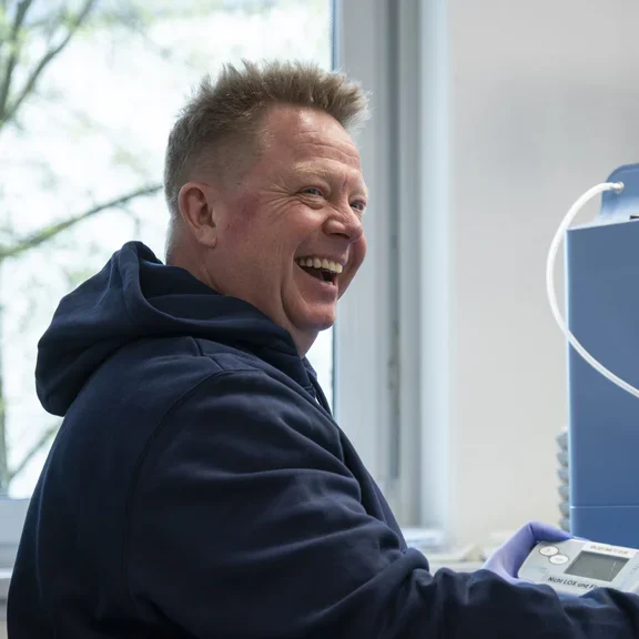 Ein Mann sitzt an einer Werkbank und lächelt