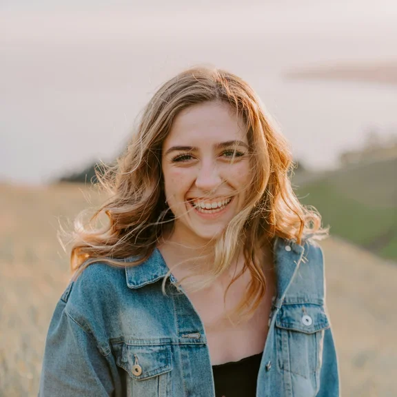 Eine Frau sitzt draußen auf einer Wiese und schaut lachend in die Kamera. 